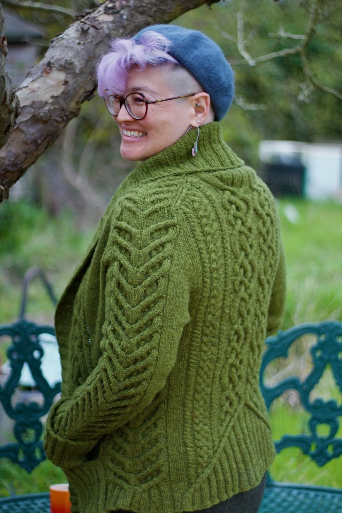 Hiroko wearing a detailed cable knit cardigan with shawl neck, smiling over her shoulder 