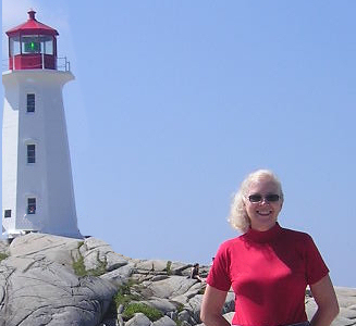 Photo of Luise O'Neill wearing sunglasses and standing in front of a lighthouse on a bright sunny day.