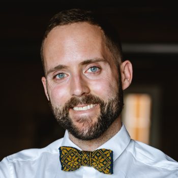Photo of Birger Berge. He wears a shirt and colourwork knitted bowtie and smiles to the camera.