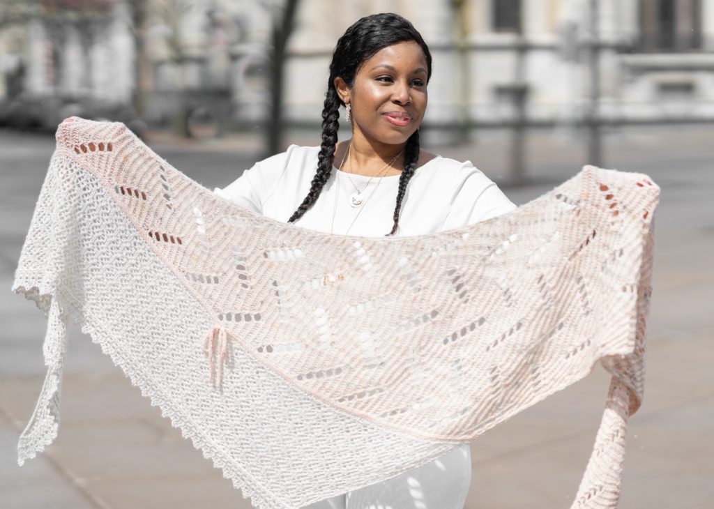 Photo of a woman holding a knitted shawl in pale pink and cream