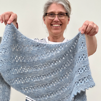 Emma Vining smiling to camera and holding up her Gentle Rain shawl